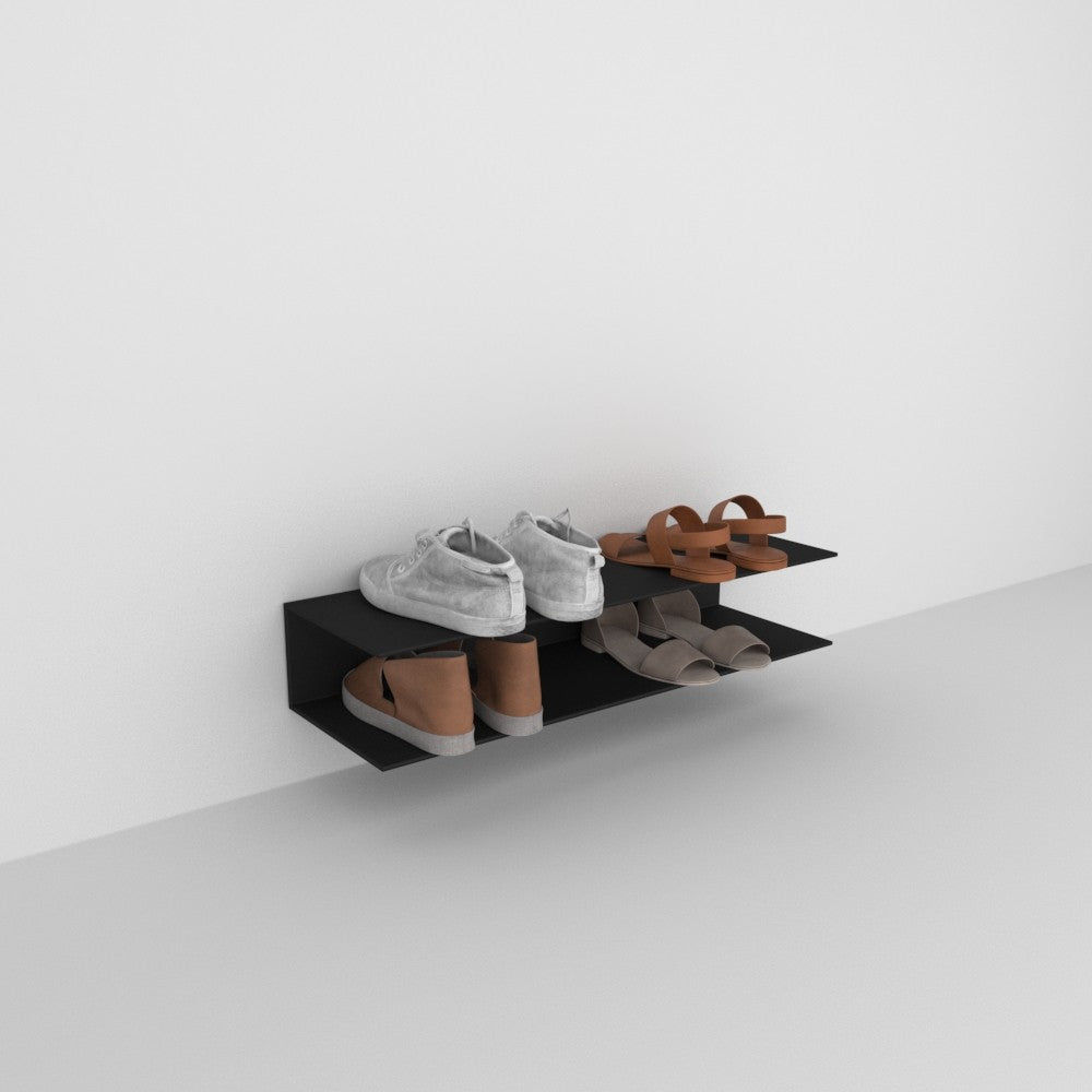 A minimalist black wall-mounted horizontal shoe rack with two shelves, showcasing a few pairs of shoes against a plain white background.