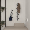 Wall-mounted tree-shaped coat racks in black metal, displayed in a modern entryway. One rack holds a jacket, while the other holds a bag, adding both function and style to the minimalist design, complemented by a neutral bench and plant decor.