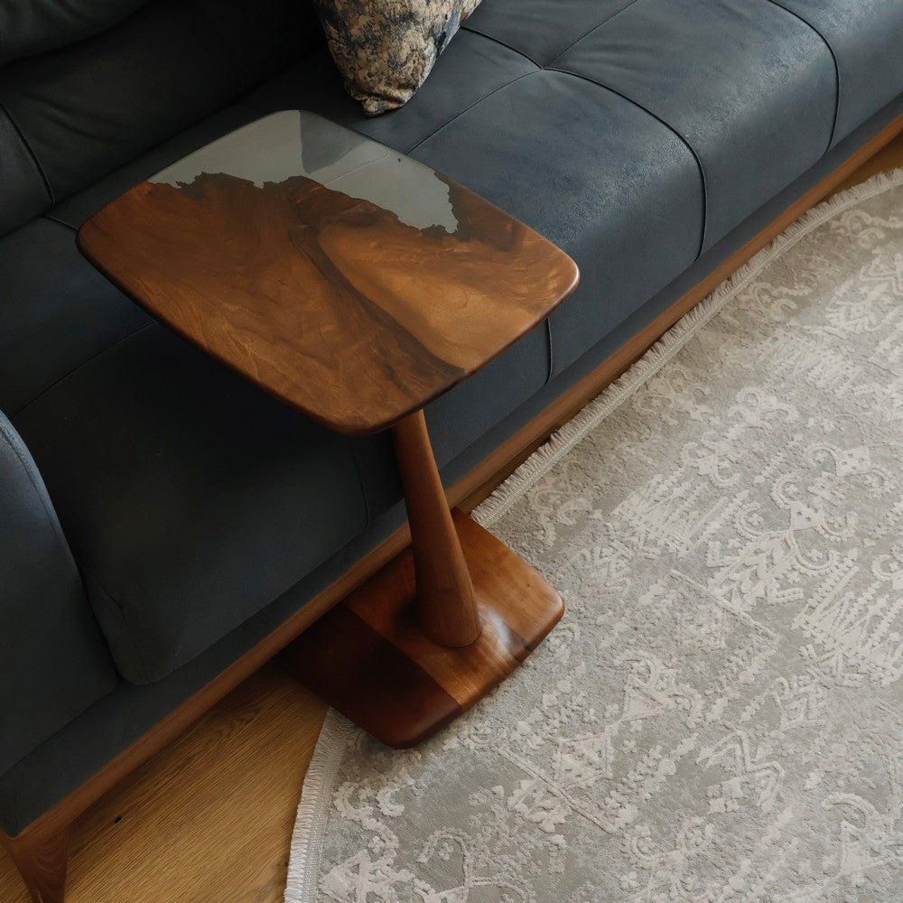 Side table with a smooth walnut wood top and resin inlay, placed beside a dark blue sofa, showing elegant craftsmanship.