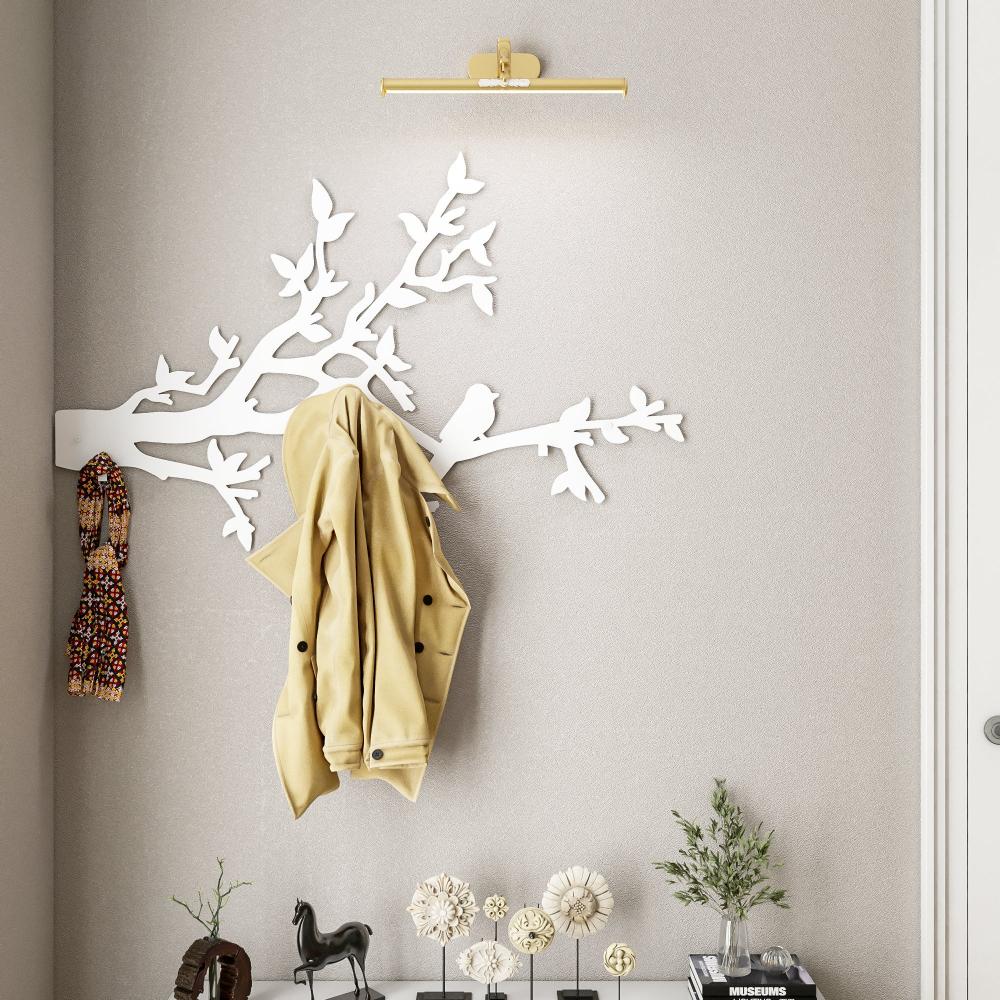 A white metal wall-mounted coat rack designed with bird and branch silhouettes. The rack holds a beige coat and a patterned scarf, providing a decorative and functional solution for hanging items in a modern entryway or living space.