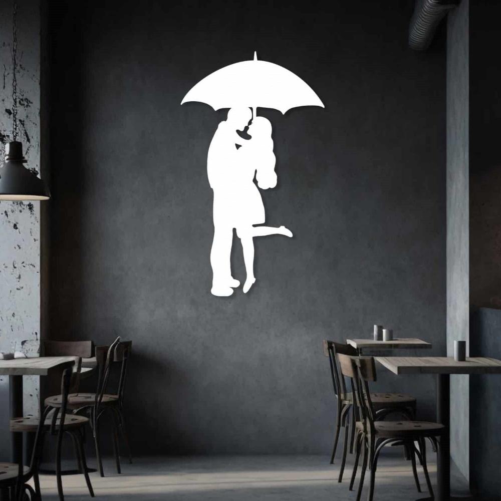 White silhouette metal wall art of a couple embracing under an umbrella, displayed on a dark modern wall, creating a romantic ambiance.