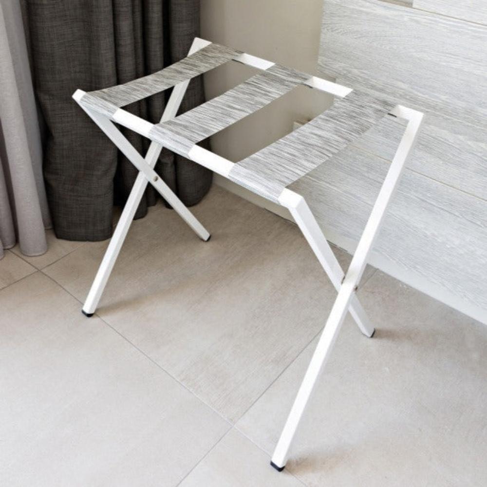 A white foldable metal luggage rack with a sleek and modern design, featuring gray straps placed in a minimalistic interior setting