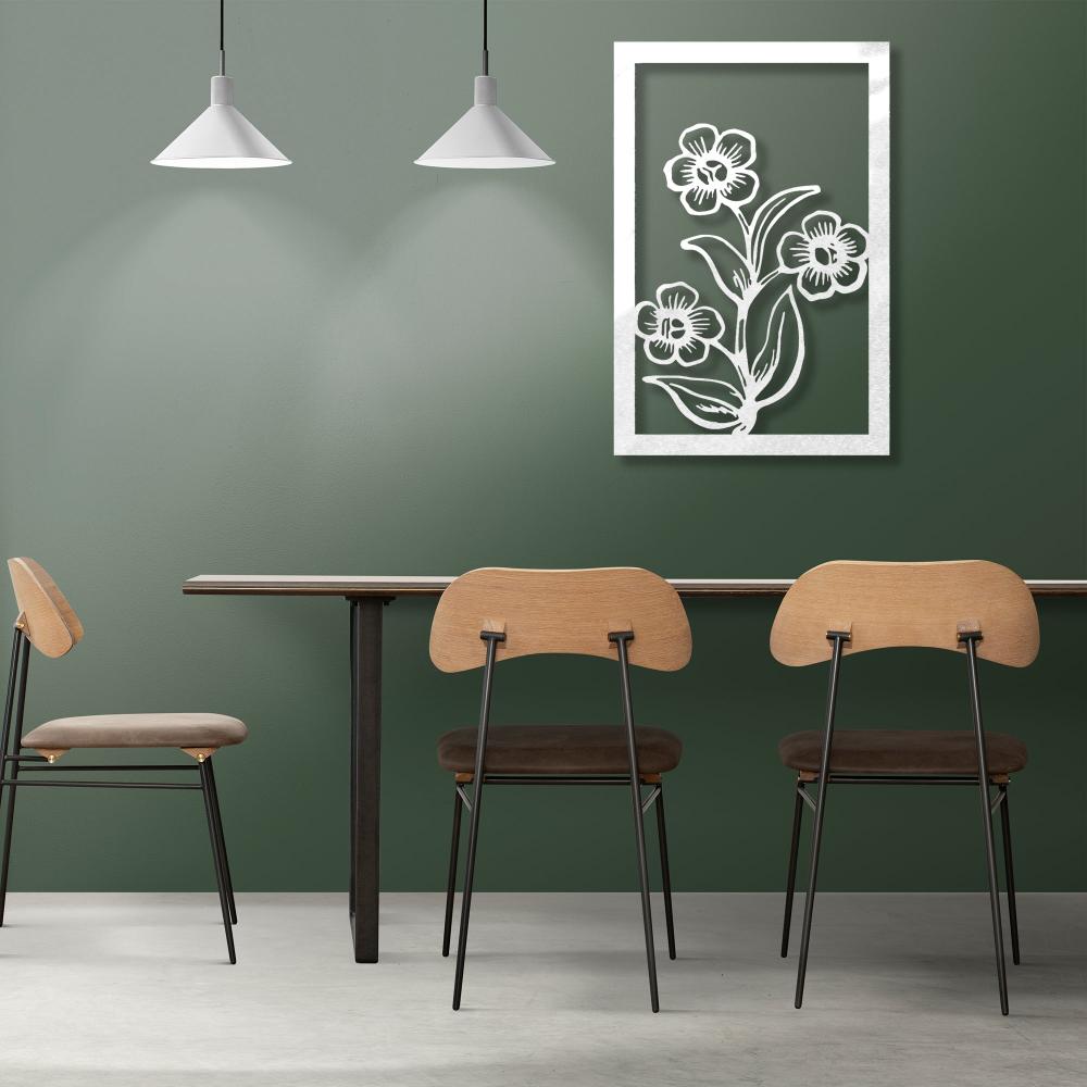 A white-painted metal floral wall art with intricate flower details, displayed on a dark green wall above a modern dining table and chairs.