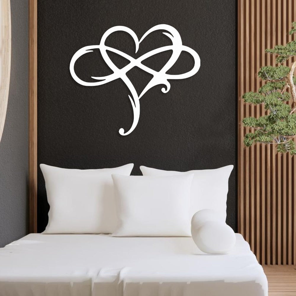 White metal heart-shaped wall art with intertwined loops, displayed above a modern minimalist bed with white pillows against a dark textured wall, complemented by wooden panel decor and a small potted tree.