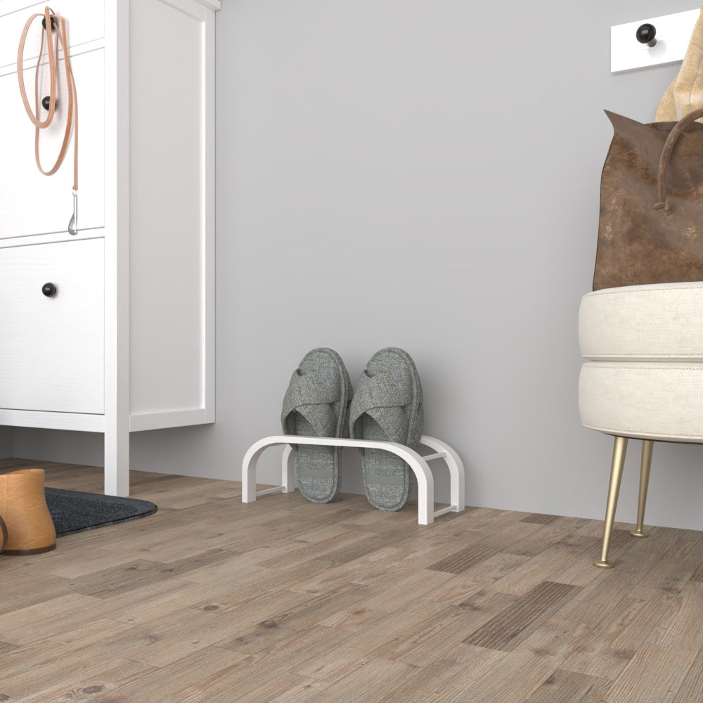 A white minimalist slipper storage rack holding a pair of gray slippers, placed in a modern hallway with wooden flooring and a white cabinet