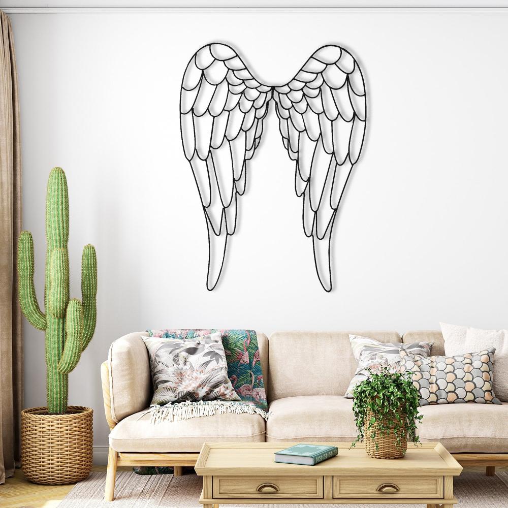 Angel wings metal wall art mounted on a bright, minimalist living room wall, surrounded by cozy decor including a tall cactus, patterned pillows, and a woven basket.