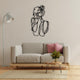 A stylish living room featuring a black metal wall art depicting a minimalist woman’s figure, mounted above a beige sofa with pink cushions.