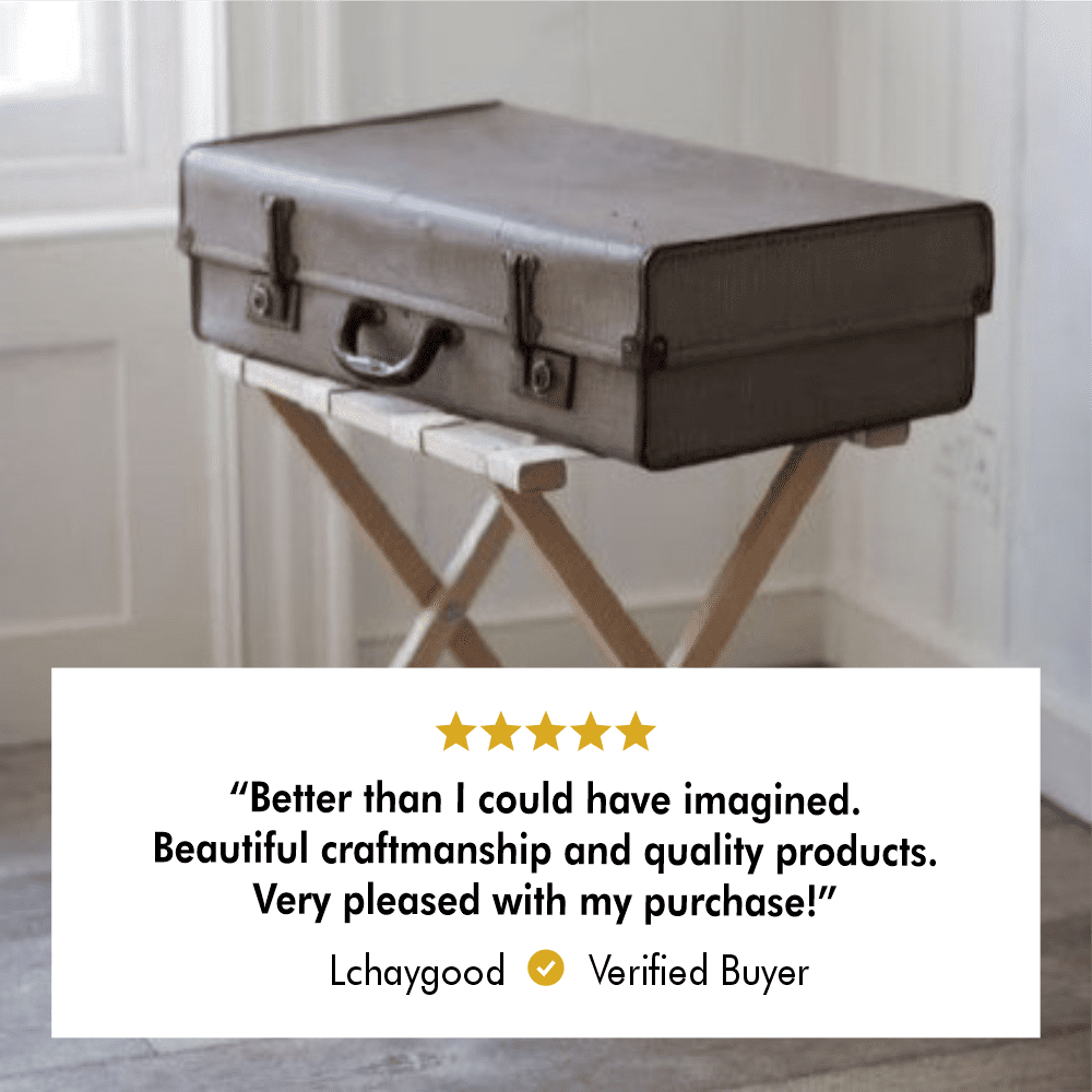 A vintage suitcase displayed on a wooden folding luggage rack in a cozy interior, accompanied by a 5-star customer review stating, "Better than I could have imagined. Beautiful craftsmanship and quality products. Very pleased with my purchase!" from a verified buyer named Lchaygood.