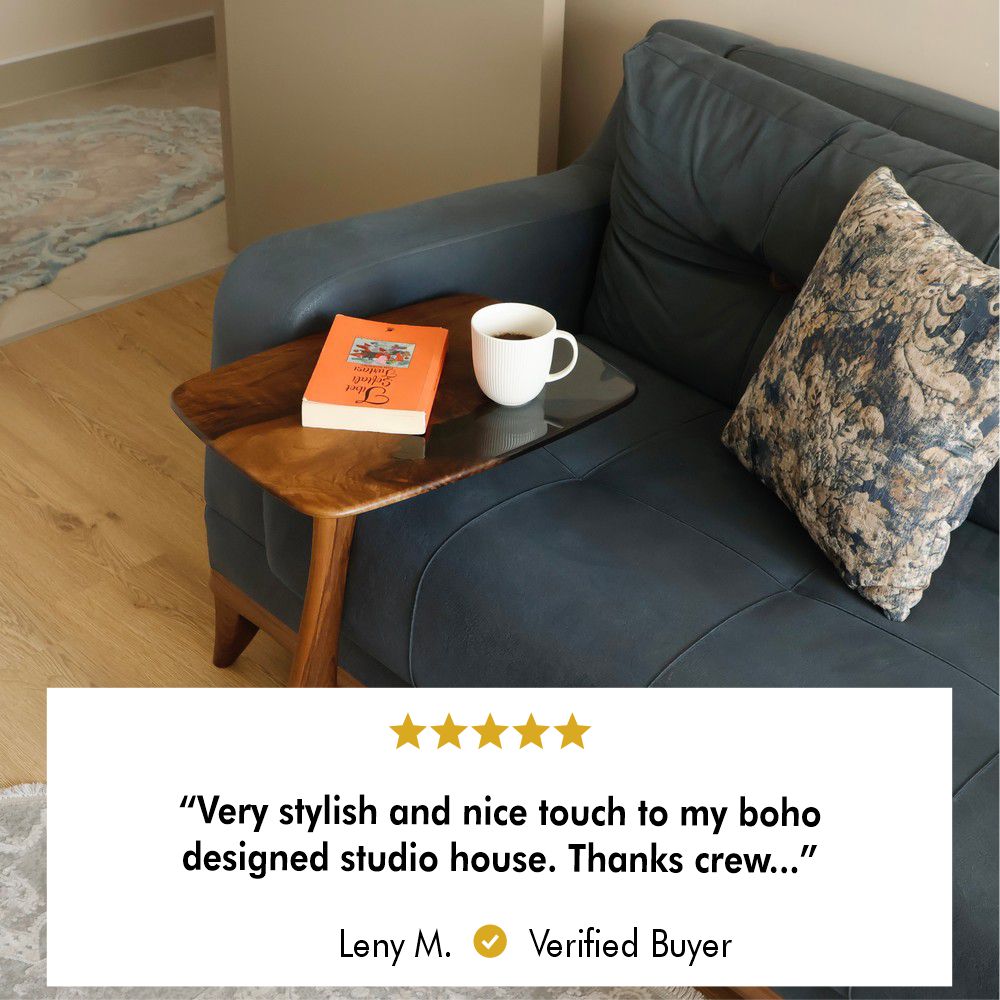 Wooden side table with resin-coated top positioned next to a dark blue sofa, holding a cup of coffee and an orange book, blending functionality with modern decor.