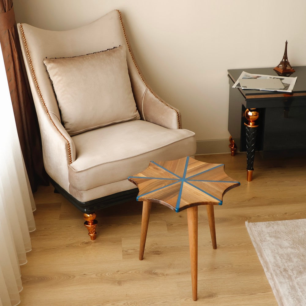 Blue-accented wooden star-shaped stool in a cozy living room setting, placed near a beige armchair and black side table.