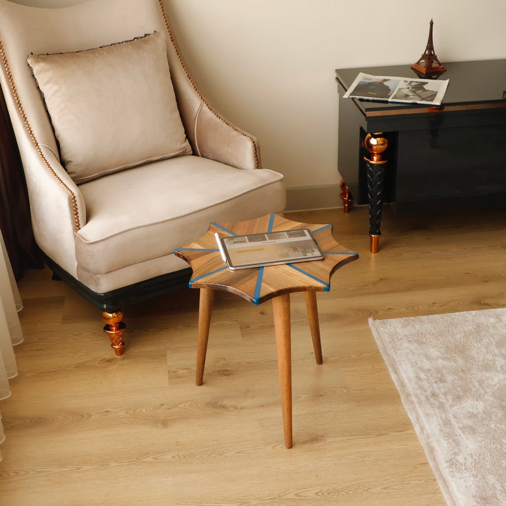 Wooden star-shaped stool with white resin inlay detail, placed in a living room with a comfortable beige chair in the background.